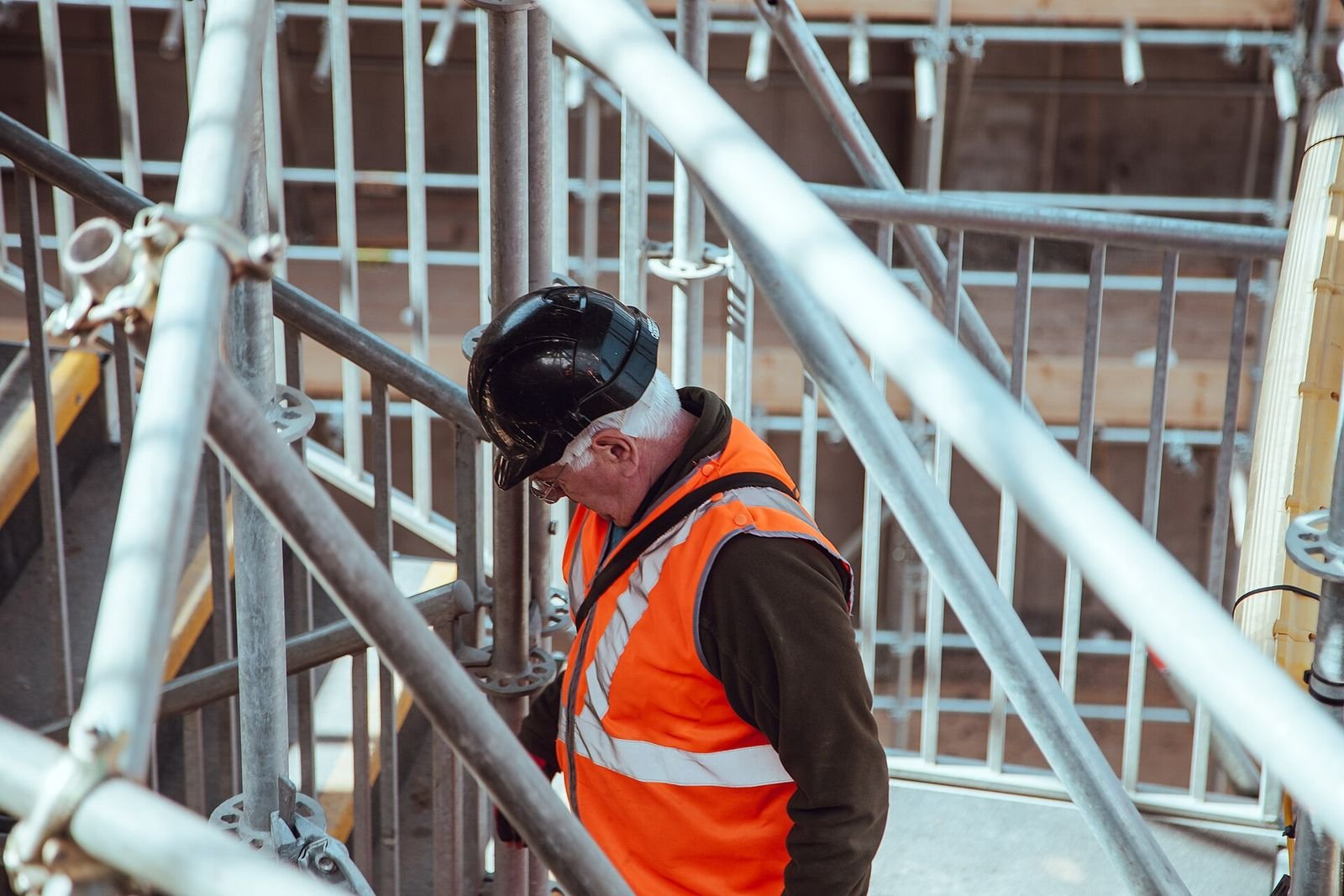 Trabalhador de capacete e colete laranja em andaime de obra de construção civil